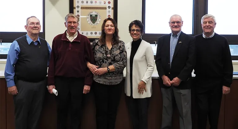 a group of smiling people standing in front of a le moyne college plaque